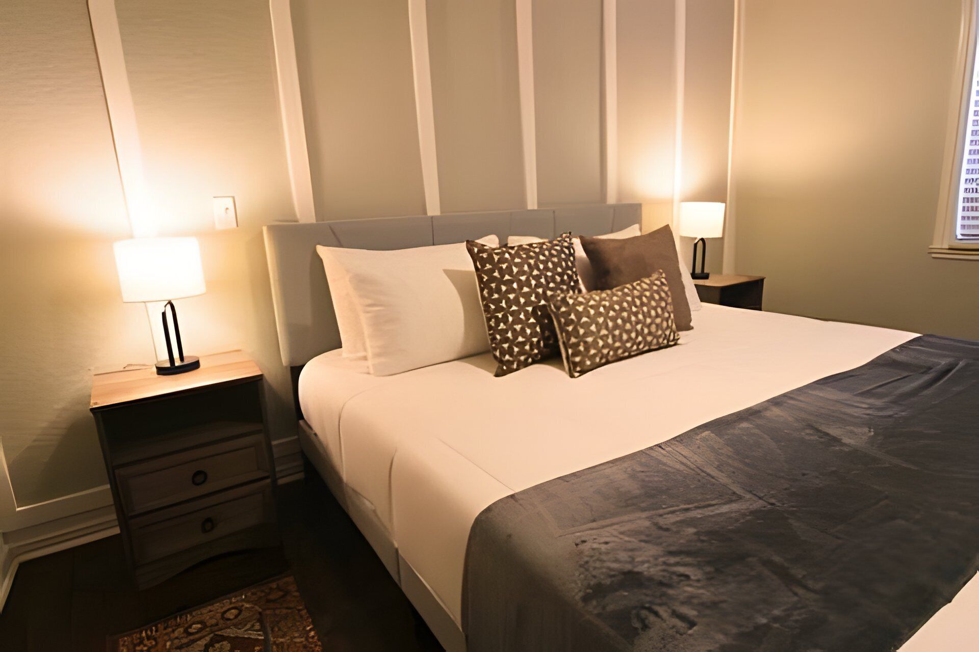 A neatly made bed with a grey blanket, two bedside tables with lamps, and a patterned pillow.