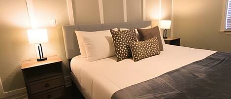 A neatly made bed with a grey blanket, two bedside tables with lamps, and a patterned pillow.