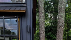 A modern building with a large glass door, a wooden deck, and a pathway surrounded by trees.