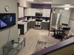 Een moderne keuken met een flatscreen-tv, roestvrijstalen apparatuur en een eethoek met een tafel en stoelen.