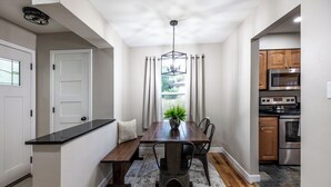A compact kitchen with modern appliances, a dining area with a wooden table and chairs, and a view through the window.