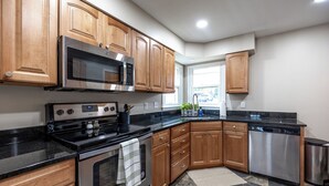 A modern kitchen with wooden cabinets, stainless steel appliances, and a black countertop.