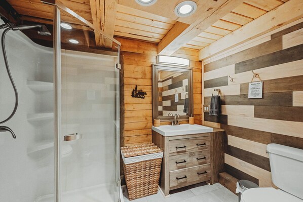 A modern bathroom with a glass shower enclosure, wooden panel walls, a white sink, and a wooden vanity with drawers.