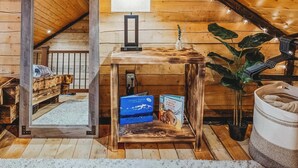 Una camera da letto mansardata accogliente, con soffitto spiovente, un letto di legno, un tavolino con una lampada e una pianta in vaso.