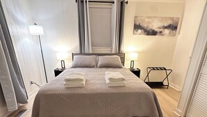 A neatly made bed with a patterned bedspread, two bedside lamps, a standing lamp, and a small table with a lamp. - Welcoming 3-bedroom house near Charlotte Airport and Uptown (Charlotte)