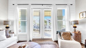 A spacious living room with a large window, a cozy sofa, a round ottoman, and a side table with a lamp. - Gulf Place 210- Steps To Beach *Snowbirds Welcome* Large Balcony (Santa Rosa Beach)