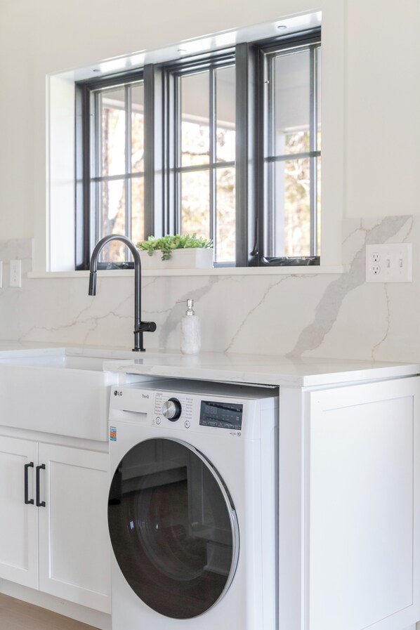A modern kitchen with a built-in washer and dryer, a window with a view, and a countertop with a faucet. - Fox Cottage – Modern Wine Country Retreat in Afton, VA (Afton)