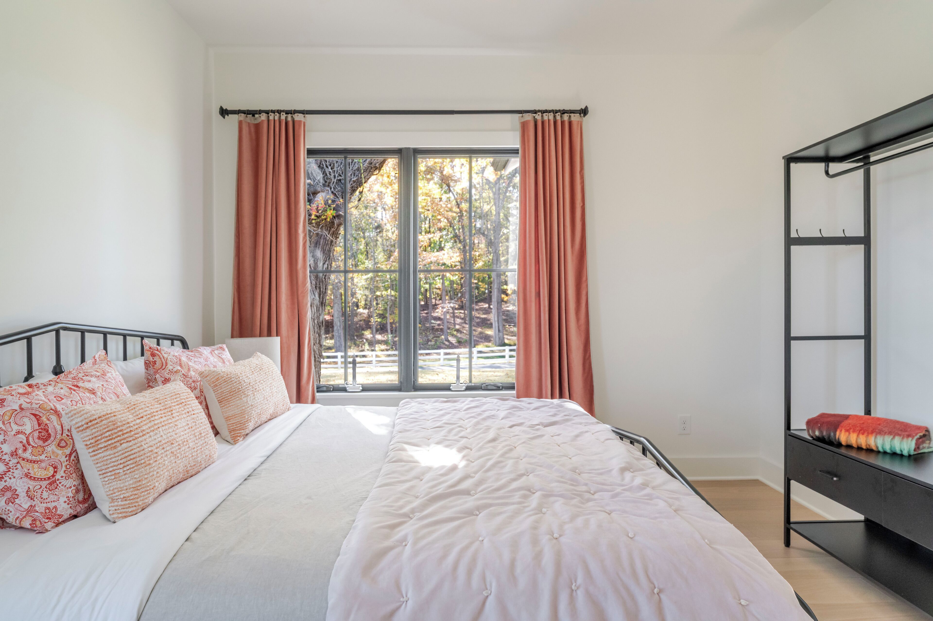 Une chambre à coucher comprenant un lit, une table de chevet, une armoire et une grande fenêtre avec des rideaux.