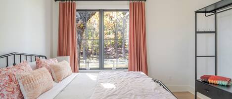 Une chambre à coucher comprenant un lit, une table de chevet, une armoire et une grande fenêtre avec des rideaux.