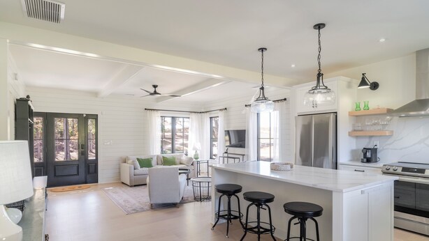 A modern kitchen with white cabinetry, a large island with bar stools, stainless steel appliances, and pendant lighting. - Fox Cottage – Modern Wine Country Retreat in Afton, VA (Afton)