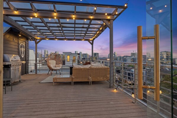 A rooftop patio with a grill, wicker furniture, and a city view.