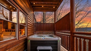 A wooden deck with a hot tub, a bench, and a view of the sunset.