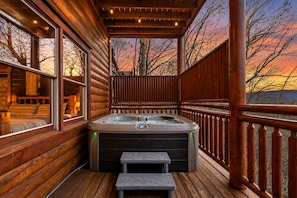 Une terrasse en bois avec un jacuzzi, un banc et une vue sur le coucher du soleil.