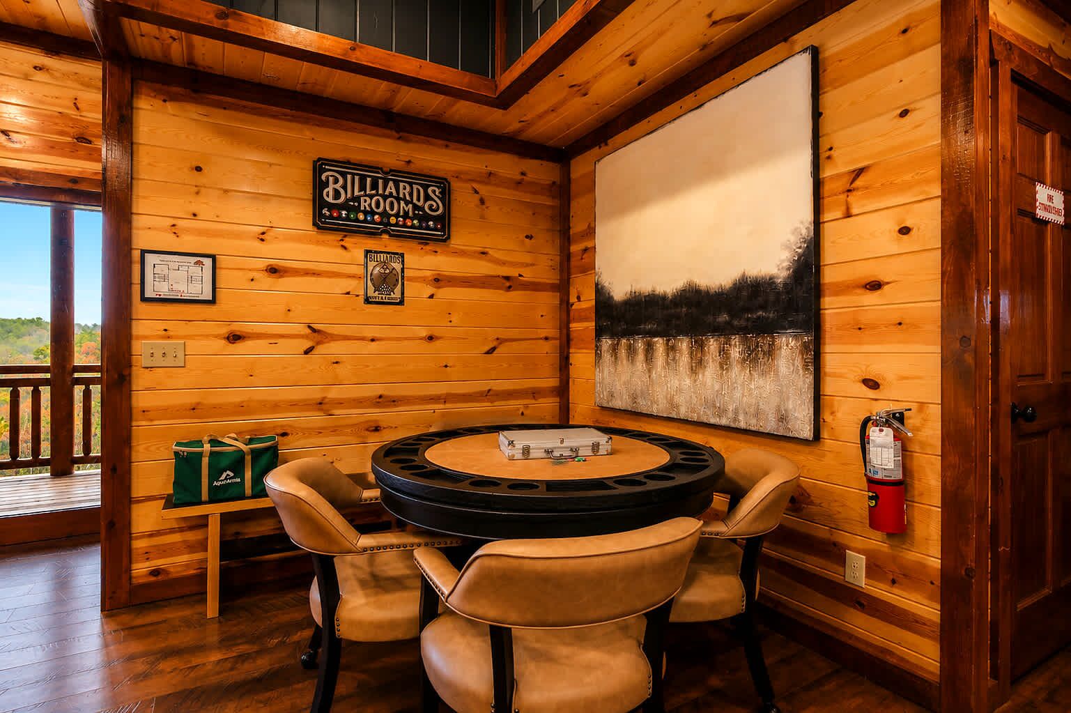 A billiards room with a billiard table, chairs, and a painting of a forest landscape.