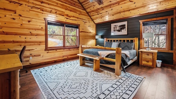 A wooden cabin bedroom with a bed, a desk, and a ceiling fan.