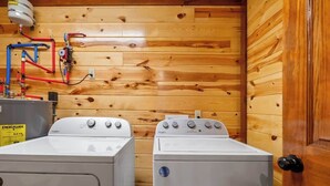 A laundry room with two Whirlpool washers, wooden walls, and visible plumbing.