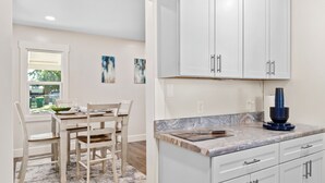 Une cuisine avec des meubles blancs, un plan de travail en marbre et un coin repas comprenant une table et des chaises.