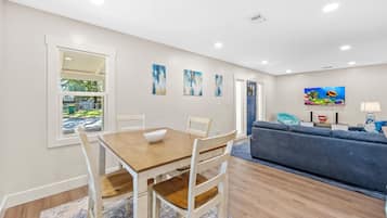 A dining area with a wooden table and white chairs, a blue couch, and a painting of fish on the wall.