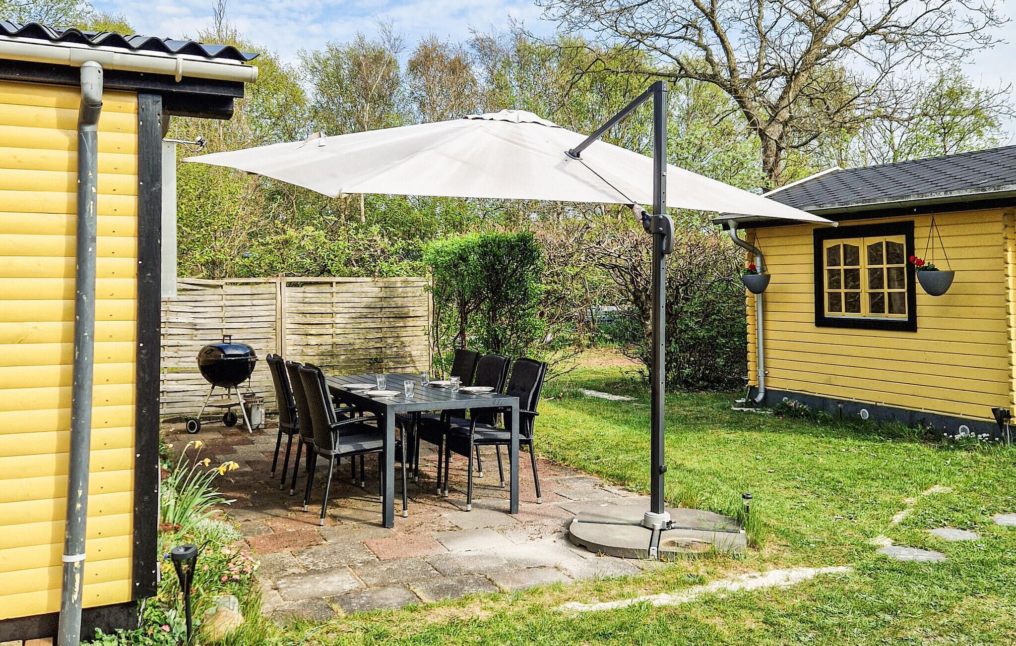 A patio with a table and chairs, a grill, and a yellow building with a window.