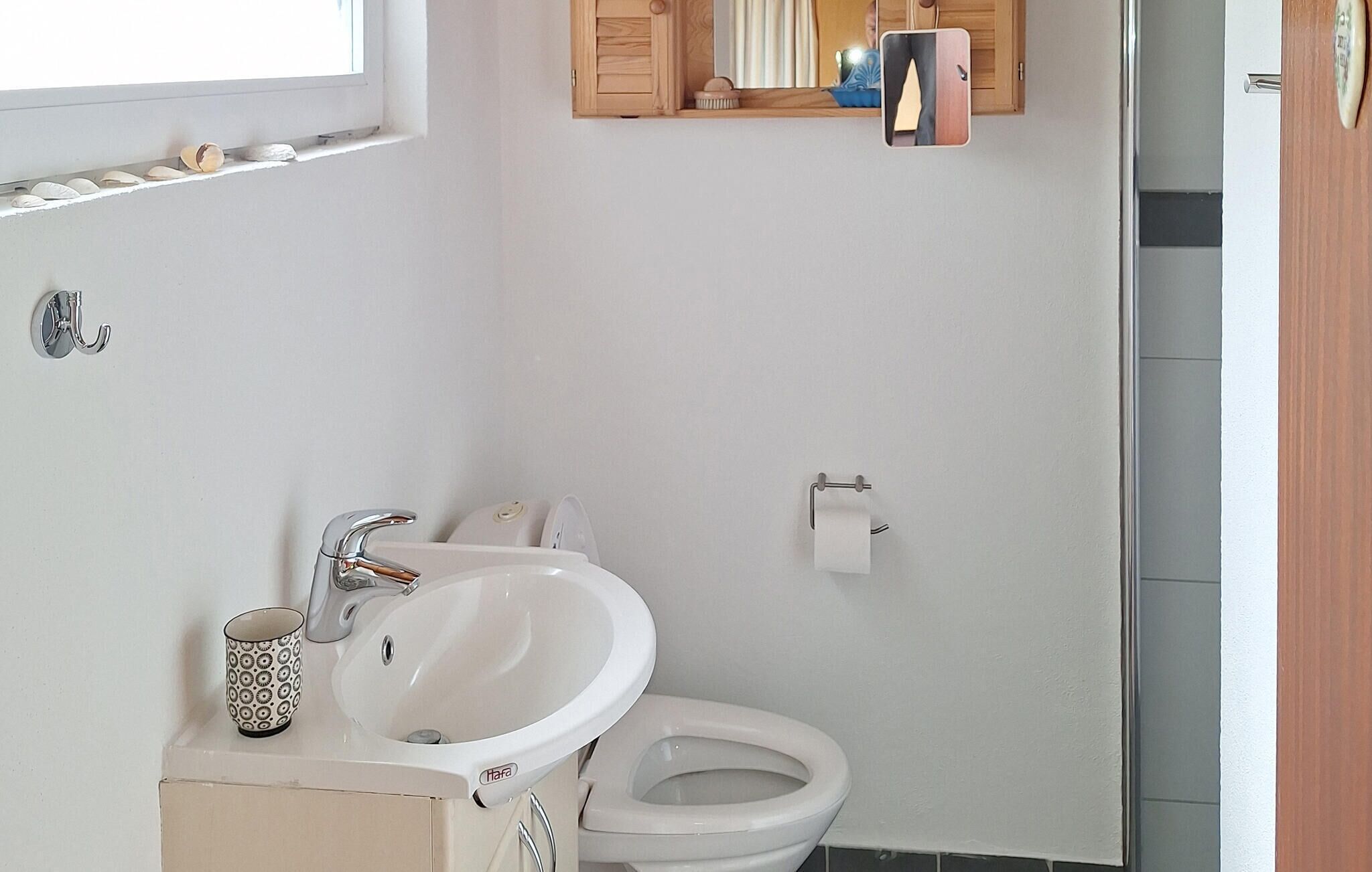 Um banheiro com pia branca, vaso sanitário, espelho e janela.