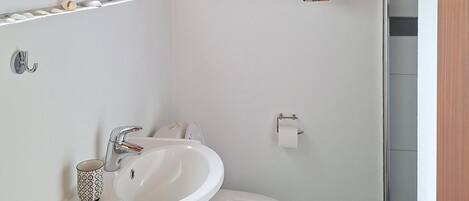 Un baño con lavamanos blanco, inodoro, espejo y ventana.