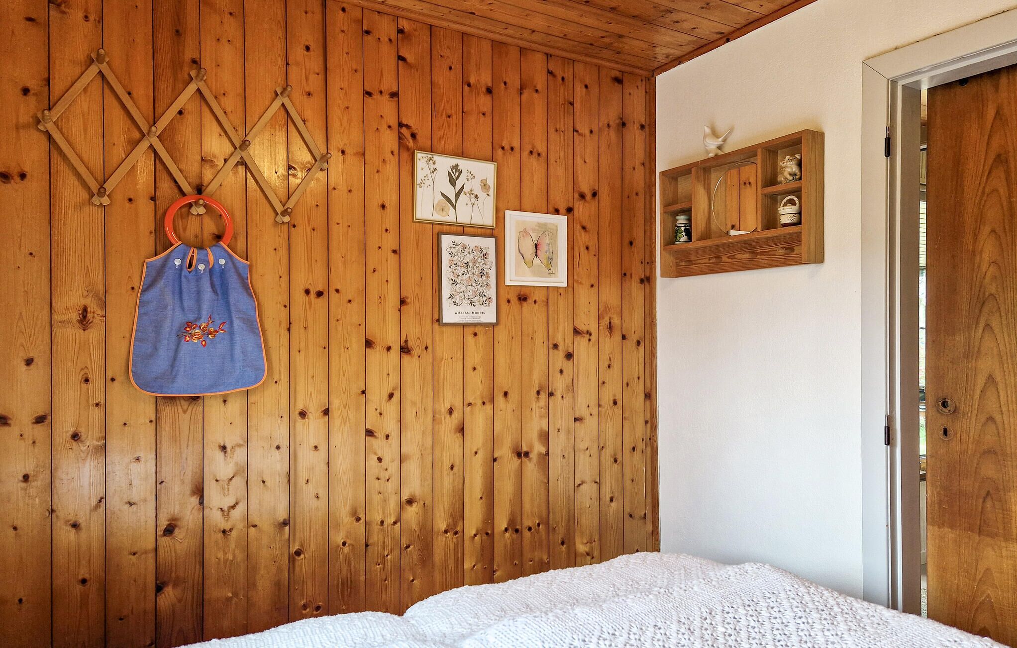 Een kamer met houten lambrisering, een bed, een wandrek en een plank met decoratieve objecten.