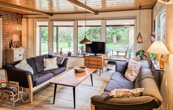 Un vaste espace de vie dotĂ© dâun plafond en bois, de grandes fenĂȘtres, dâun tĂ©lĂ©viseur et dâune table Ă manger.