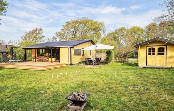 A yellow cabin with a deck, a fire pit, and a covered patio area.