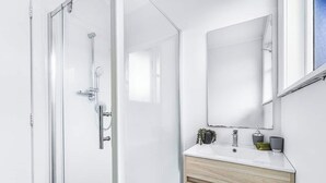 A modern bathroom with a glass shower enclosure, a white vanity with a mirror, and a small potted plant. - 3-Bedroom House +Private yard+sliding gate (Hamilton)