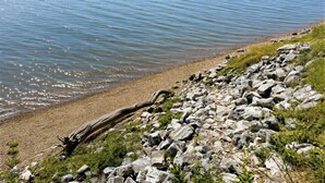 A lakeside view with a rocky shoreline, calm water, and distant forested land. - Waterfront Luxury - Hot Tub, Game Room, Kayaks, Best View (Cadiz)