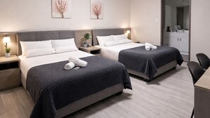 A hotel room with two beds, a desk, a mirror, and artwork on the walls. - Banksia Motel Bass Hill (Bass Hill)