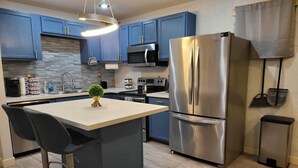 Cozinha moderna com armários azuis, uma geladeira de aço inoxidável e uma ilha central com banquetas.