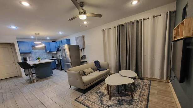 Uma sala de estar moderna com um sofá, duas mesinhas, um tapete estampado e um ventilador de teto.