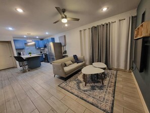 Ein modernes Wohnzimmer mit einer Couch, zwei kleinen Tischen, einem gemusterten Teppich und einem Deckenventilator.