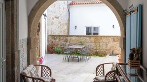 An outdoor patio with a stone wall, a table with chairs, and a view of a building with a red-tiled roof. - Rustic & Modern Stone House by Host Wise (Pedroso)