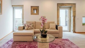 A modern living room with a beige sofa, a glass coffee table with a potted orchid, and a pink shag rug. - Rustic & Modern Stone House by Host Wise (Pedroso)