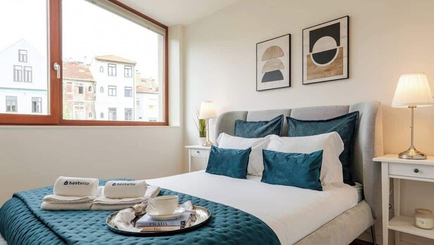 A hotel room with a bed, a window, a bedside table, and a lamp.