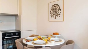 A compact kitchen with a stove, oven, and dining table set for breakfast with plates, bowls, and a cake.