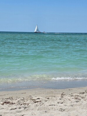 Une plage avec un voilier à l’horizon et des empreintes de pas qui mènent à l’eau.