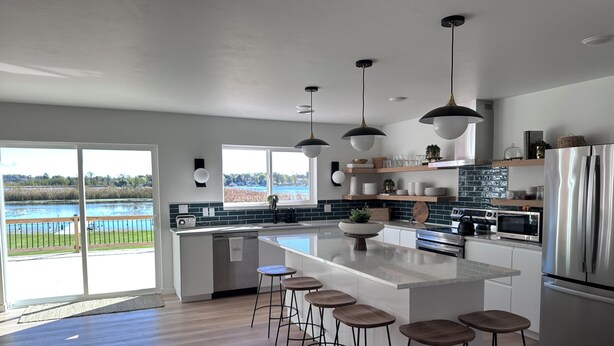 A modern kitchen with a large island, bar stools, stainless steel appliances, and a view of a lake.