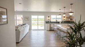 A modern kitchen with a central island, bar stools, pendant lighting, and a view of the outdoors through large windows.