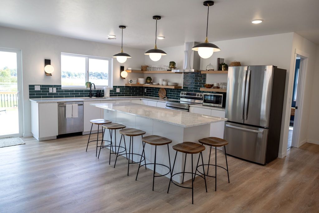 A modern kitchen with a large island, bar stools, stainless steel appliances, and pendant lighting.