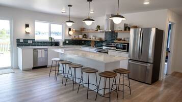 A modern kitchen with a large island, bar stools, stainless steel appliances, and pendant lighting.