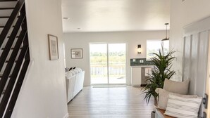 A spacious hallway with a dark floor, a staircase on the left, and a kitchen area with a plant and a bench on the right.