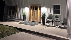 A two-story house with a front porch, a wooden door, and two potted plants.
