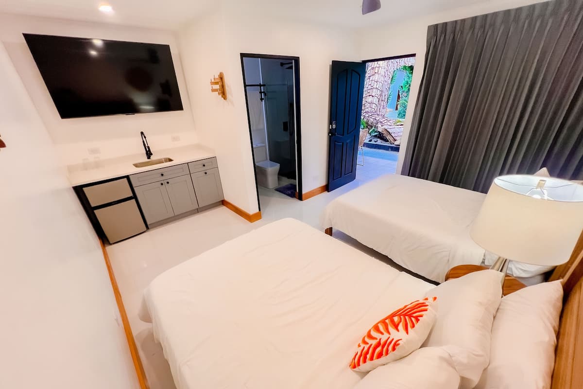 A hotel room with two beds, a TV, a sink, and a view of the outside.