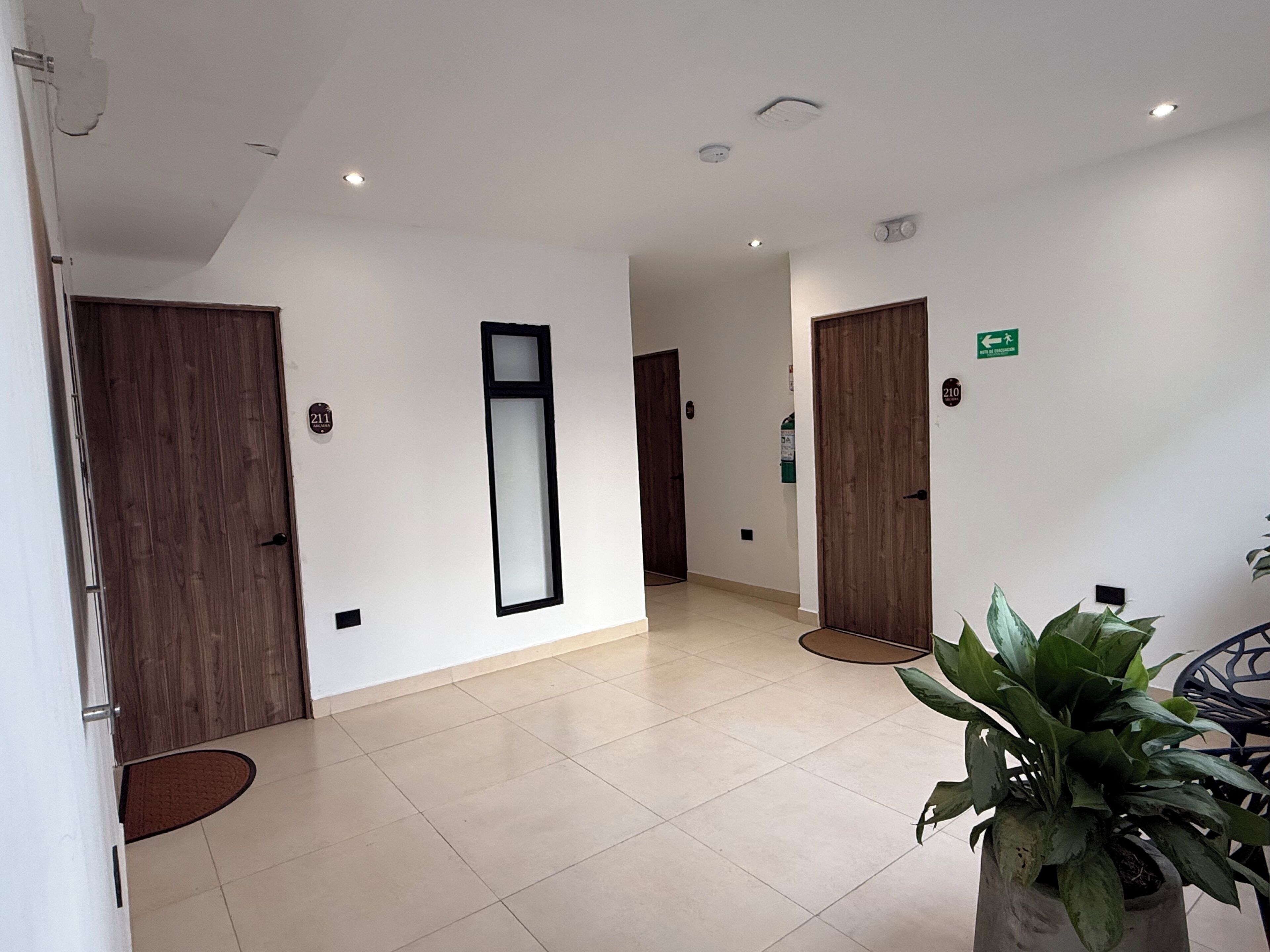 A hotel lobby with a reception desk, wooden doors, a large mirror, and a potted plant.