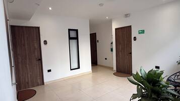 A hotel lobby with a reception desk, wooden doors, a large mirror, and a potted plant.