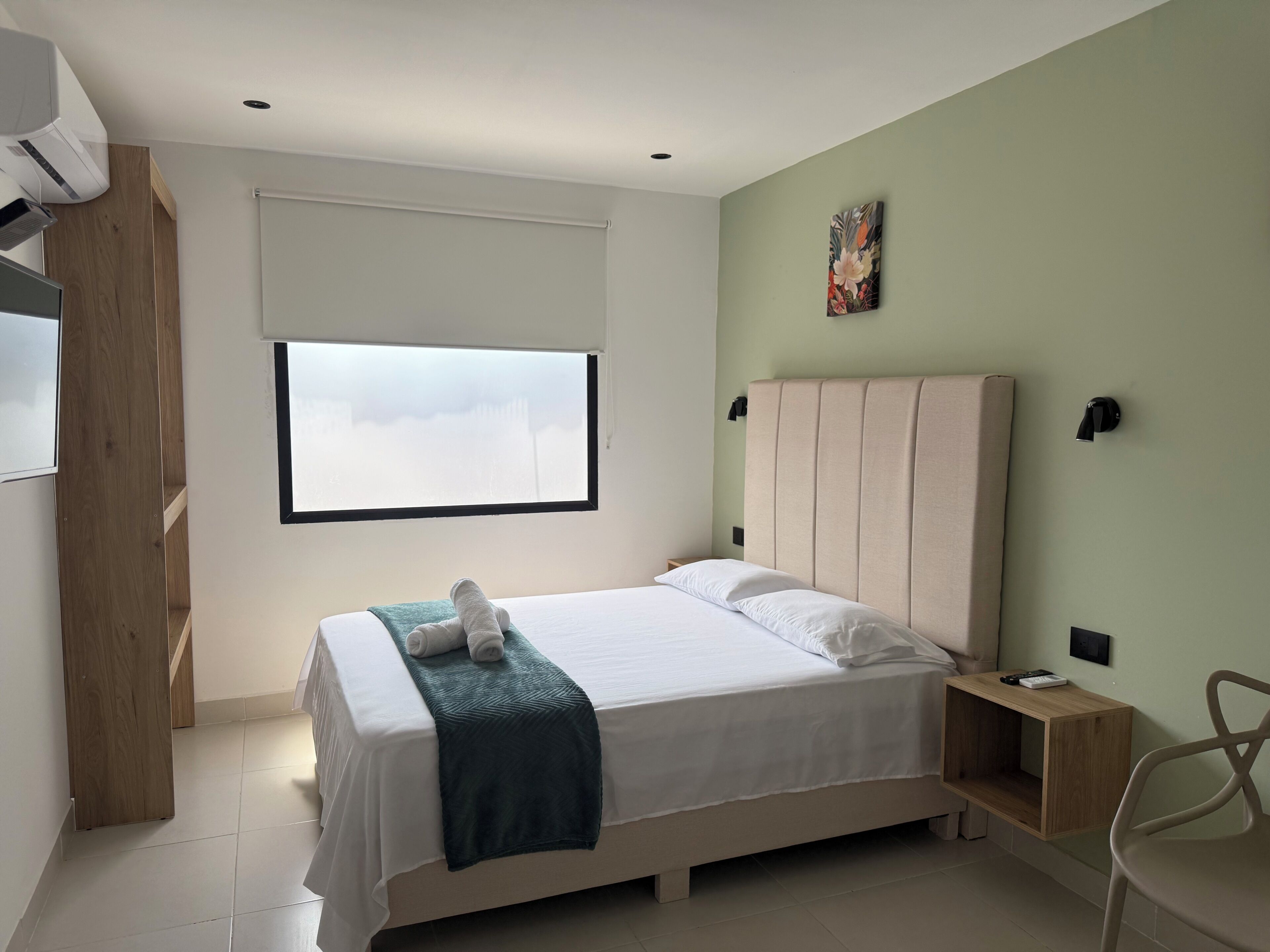 A bedroom with a bed, a window, a wall-mounted artwork, and a bedside table.