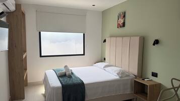 A bedroom with a bed, a window, a wall-mounted artwork, and a bedside table.